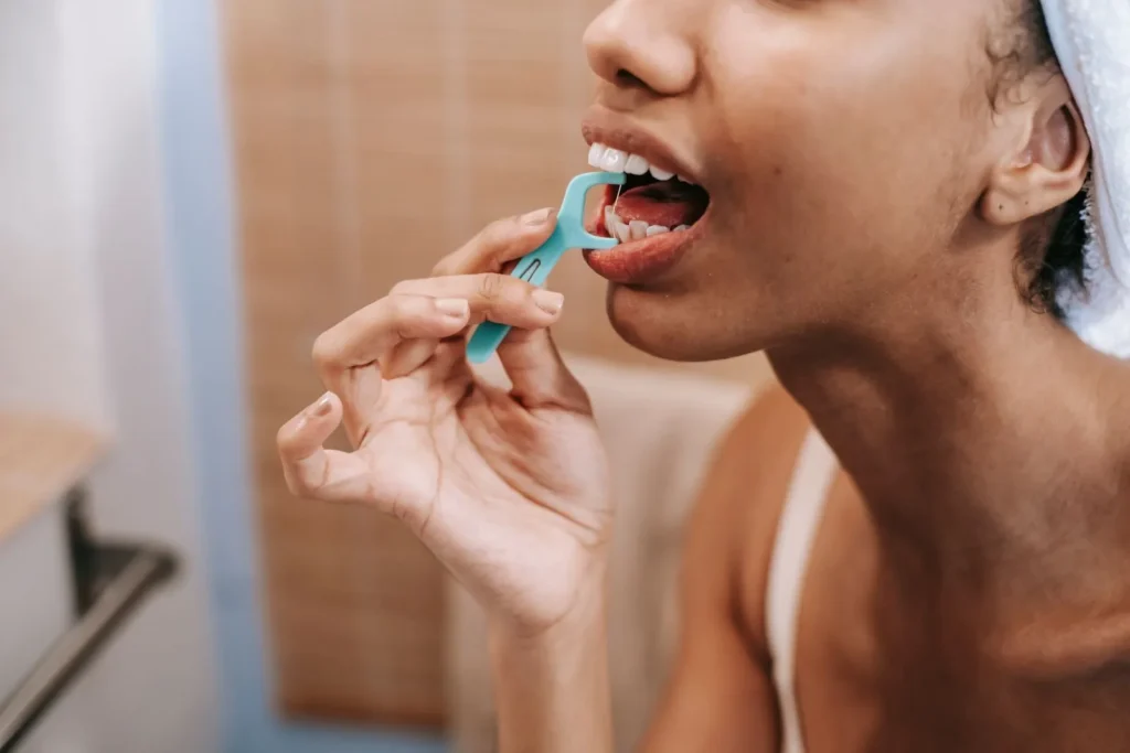 Adult using a dental floss pick in front of a bathroom mirror at home in soft natural light