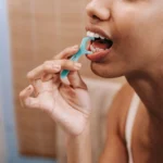 Adult using a dental floss pick in front of a bathroom mirror at home in soft natural light